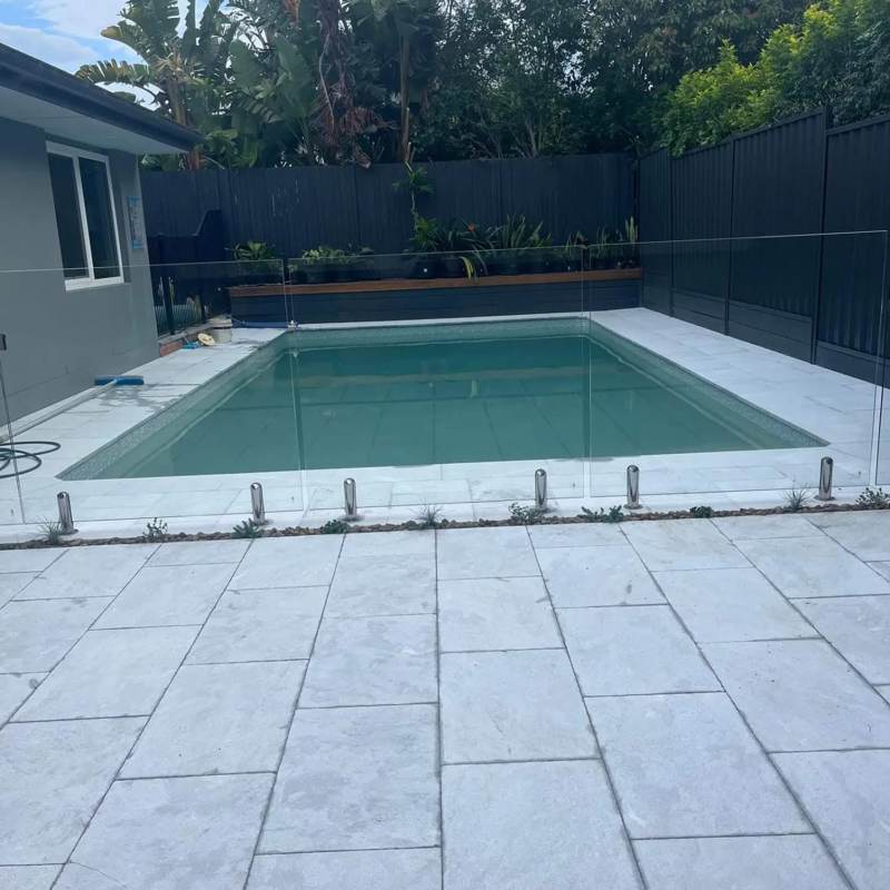 Pool surround with light stone paving and glass pool fencing